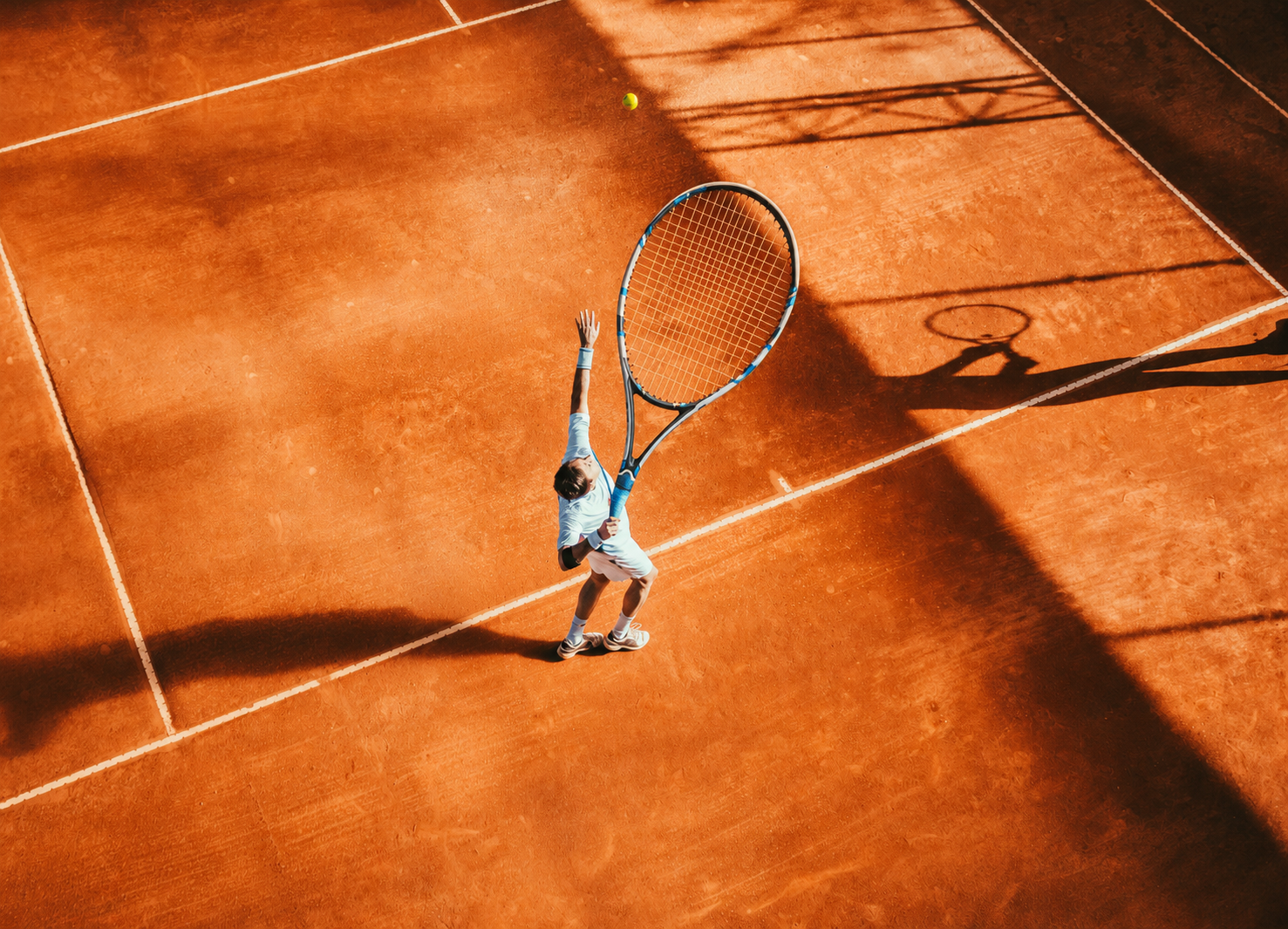 Tennis player serving on a sunlit clay court